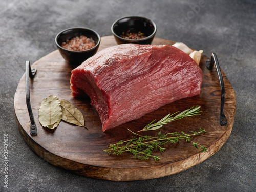 Piece of raw rump steak prepared with spices on wooden board over grey background. photo