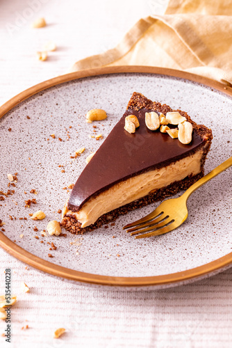 vegan peanut butter no bake tart slice on a plate with crushed peanuts as a decoration with golden fork close up