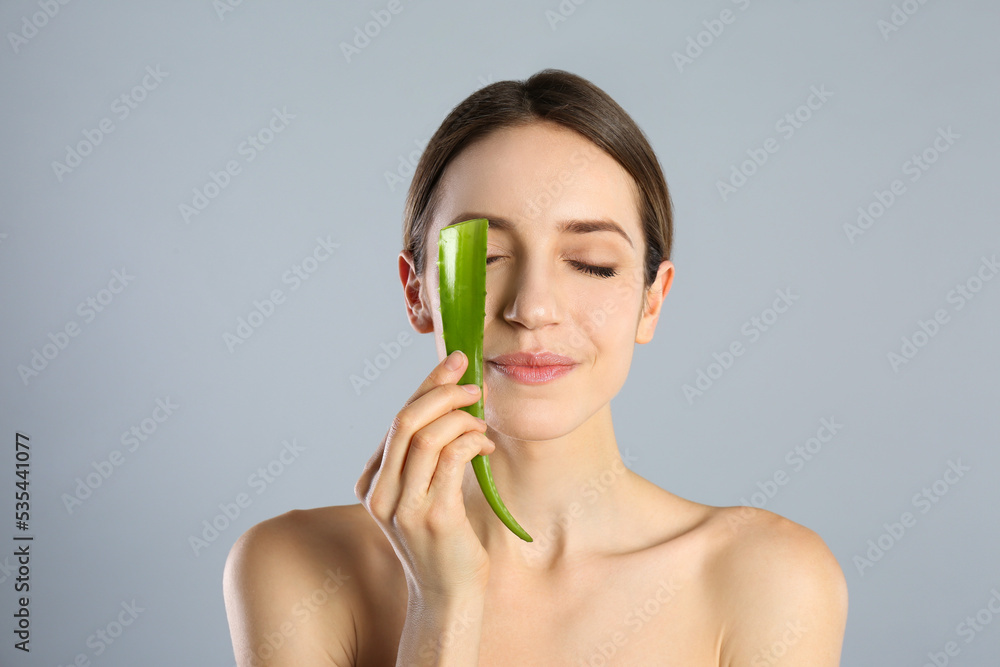Young woman with aloe leaf on light grey background Young woman with aloe leaf on light grey background