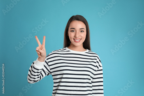 Woman showing number two with her hand on light blue background