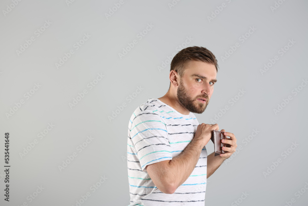 Greedy young man hiding wallet with money on light grey background, space for text Greedy young man hiding wallet with money on light grey background, space for text
