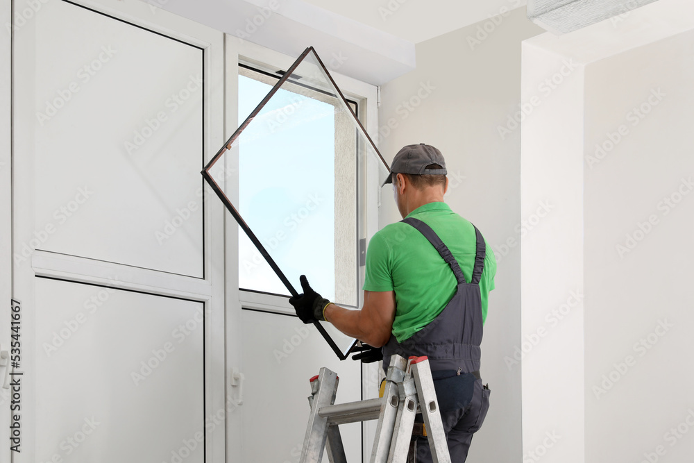 Worker on folding ladder installing window indoors Worker on folding ladder installing window indoors
