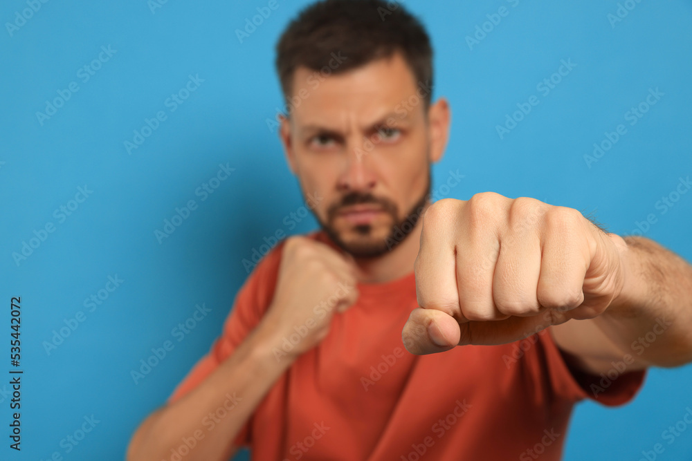 Man throwing punch against light blue background, focus on fist. Space for text Man throwing punch against light blue background, focus on fist. Space for text