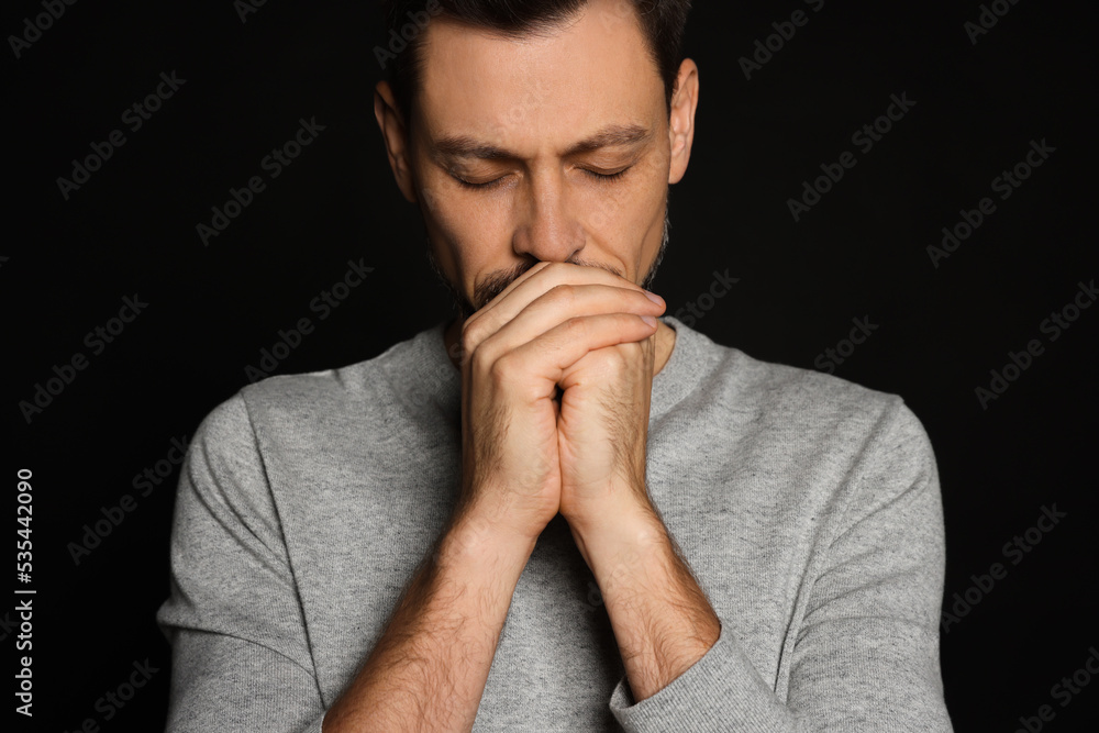 Man with clasped hands praying on black background Man with clasped hands praying on black background