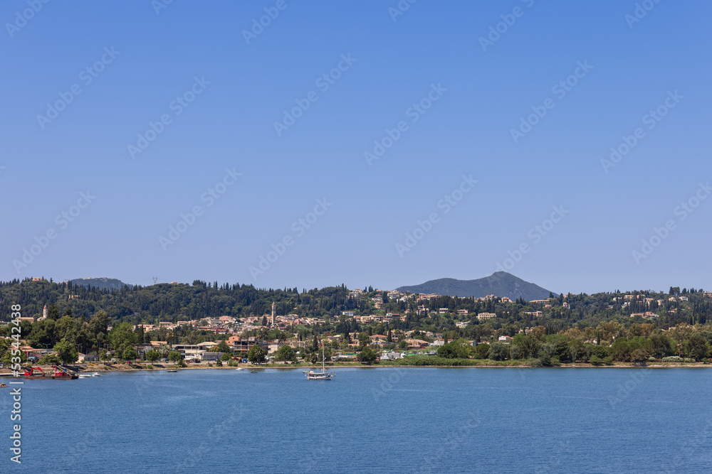 The coastline of Corfu island with urban areas immersed in lush greenery all year round, under blue clear morning sky, Ionian islands, Greece