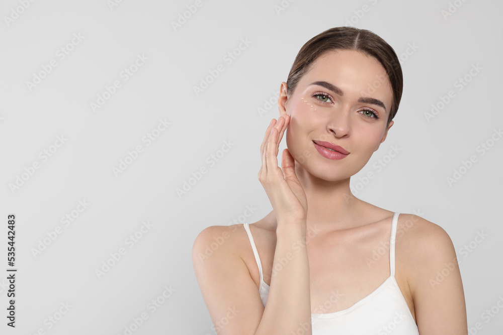 Young woman with cream around eye on white background, space for text