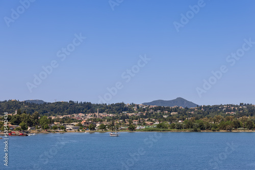The coastline of Corfu island with urban areas immersed in lush greenery all year round, under blue clear morning sky, Ionian islands, Greece
