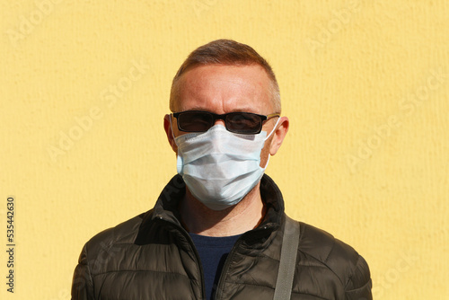 Portrait of a man in sunglasses and a medical mask on a yellow background. The concept is the epidemic of coronavirus.