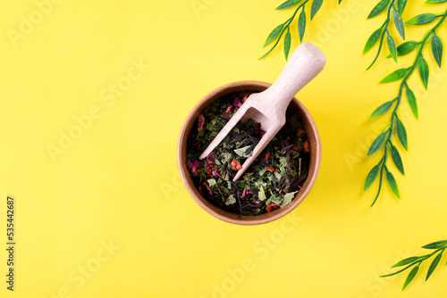 Fireweed tea or Ivan Chai with currant leaf and berries, apple, rosehip and rose petals in paper cup with wooden scoop on yellow background. Top view photo