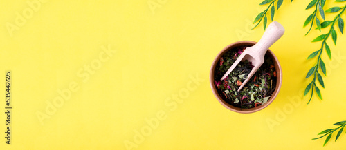 Web banner with fireweed tea or Ivan Chai with currant leaf and berries, apple, rosehip and rose petals in paper cup with wooden scoop on yellow background. Mockup with copy space photo