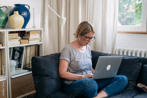 mid adult woman sits on sofa in living room and using laptop computer