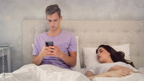 Man Chatting on Phone While Girl is Sleeping. Man Using Phone in Bed. Girl Sleeping in bed. Shot on RED photo