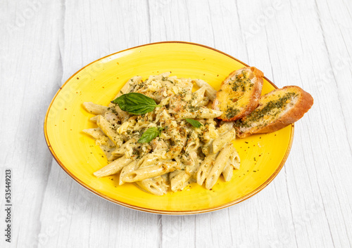 Closeup of a delicious pasta dish with heavy seasoning, bread and basils on a yellow plate photo