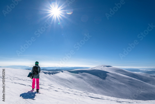 Snowboarder woman with snowboard in hand on mountain top. Winter freeride snowboarding