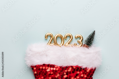 New year 2023 number, golden digits and santa hat over blue background. © gitusik