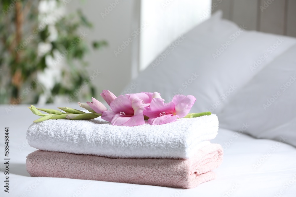 Terry towels with beautiful flower on bed indoors, space for text Terry towels with beautiful flower on bed indoors, space for text