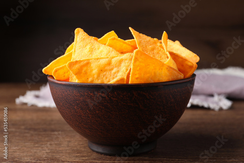 Tortilla chips (nachos) in bowl on wooden table against dark background, closeup