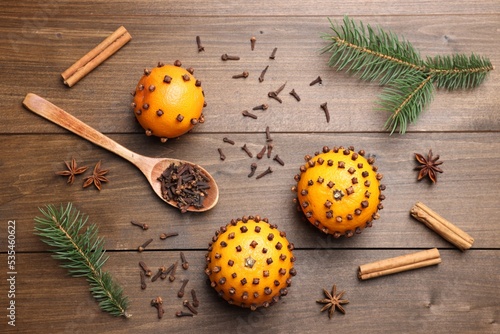 Pomander balls made of tangerines with cloves and fir branches on wooden table, flat lay