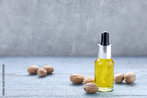 Bottle of nutmeg oil and nuts on grey wooden table. Space for text