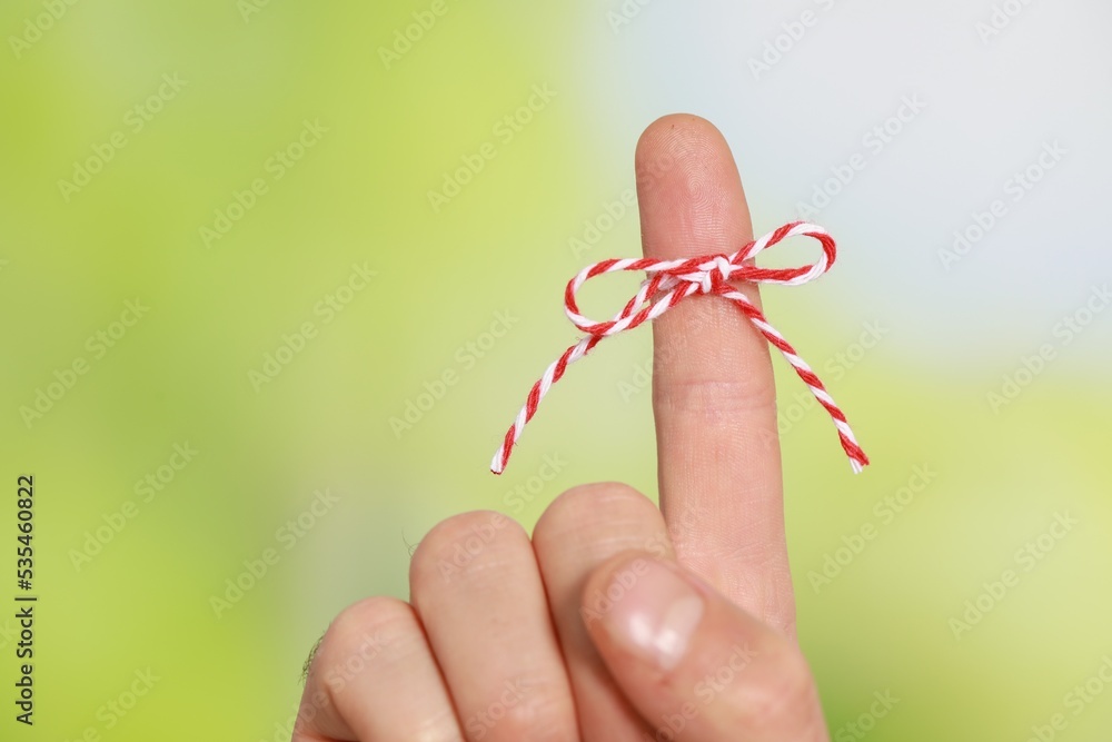 Man showing index finger with tied bow as reminder on green blurred background, closeup Man showing index finger with tied bow as reminder on green blurred background, closeup