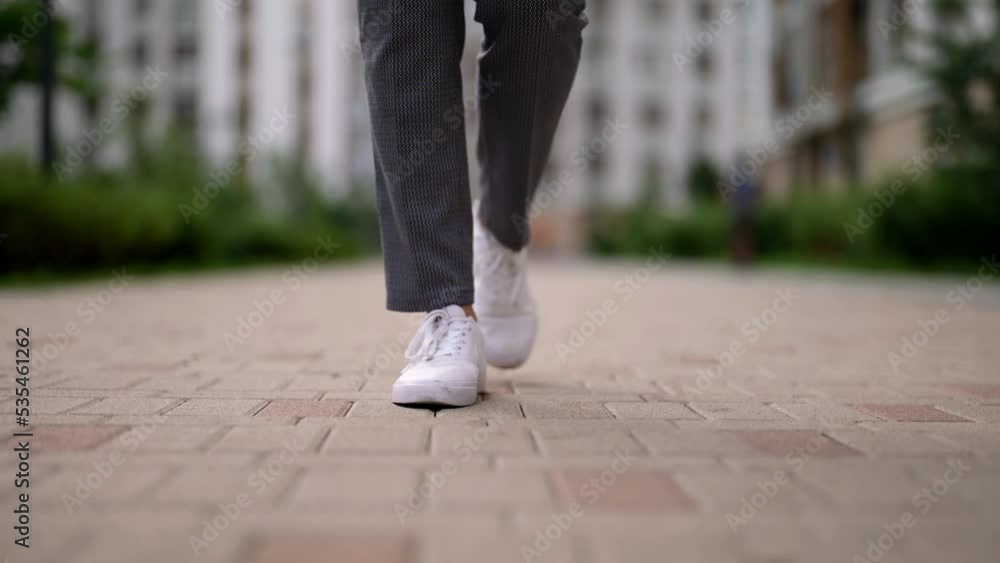 casual dressed woman walking on tiled path in city center, checked pants and white sneakers, closeup casual dressed woman walking on tiled path in city center, checked pants and white sneakers, closeup