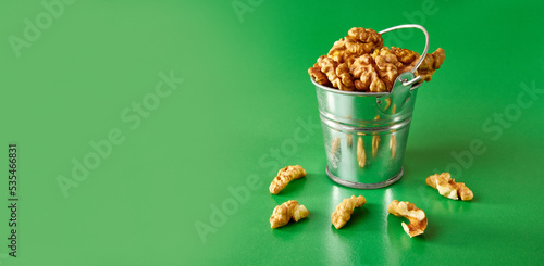 A small metal bucket filled with walnuts on a green background. Concept of healthy eating.