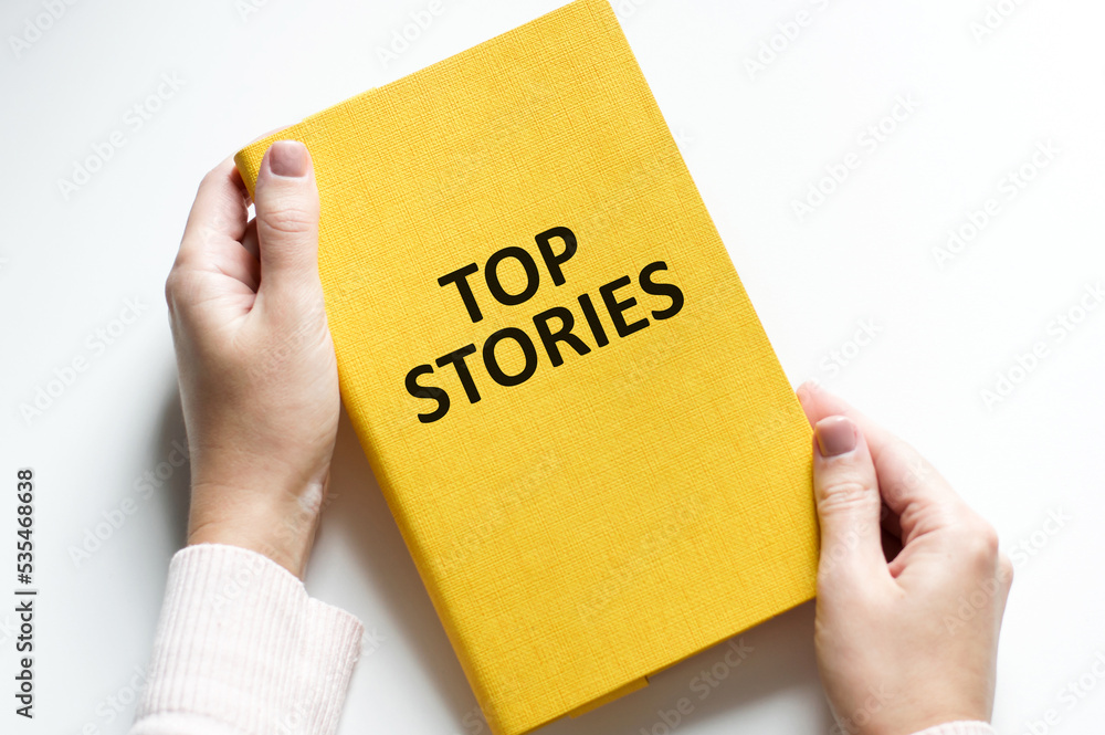 Word TOP STORIES on the cover of a yellow notebook in a person's hand on a light background Word TOP STORIES on the cover of a yellow notebook in a person's hand on a light background