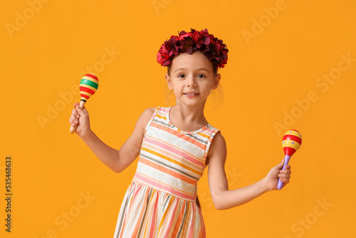 Little Mexican girl with floral wreath and maracas on yellow background photo