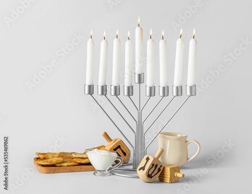 Menorah with candles, potato pancakes, sauce and dreidels for Hanukkah celebration on grey background photo