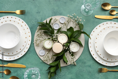 Elegant table setting with beautiful floral decor and candles on green background