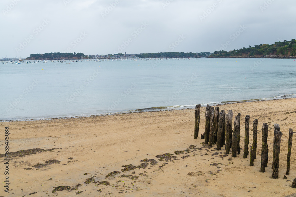 Row of vertical trunks on the sand in the beach of Dinard, Brittany, France, with the blue waters of atlantic ocean. Gray overcasted sky on the background.