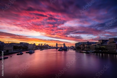 Colorful sunrise behind the skyline of London, England, with Tower Bridge and reflections in the river Thames