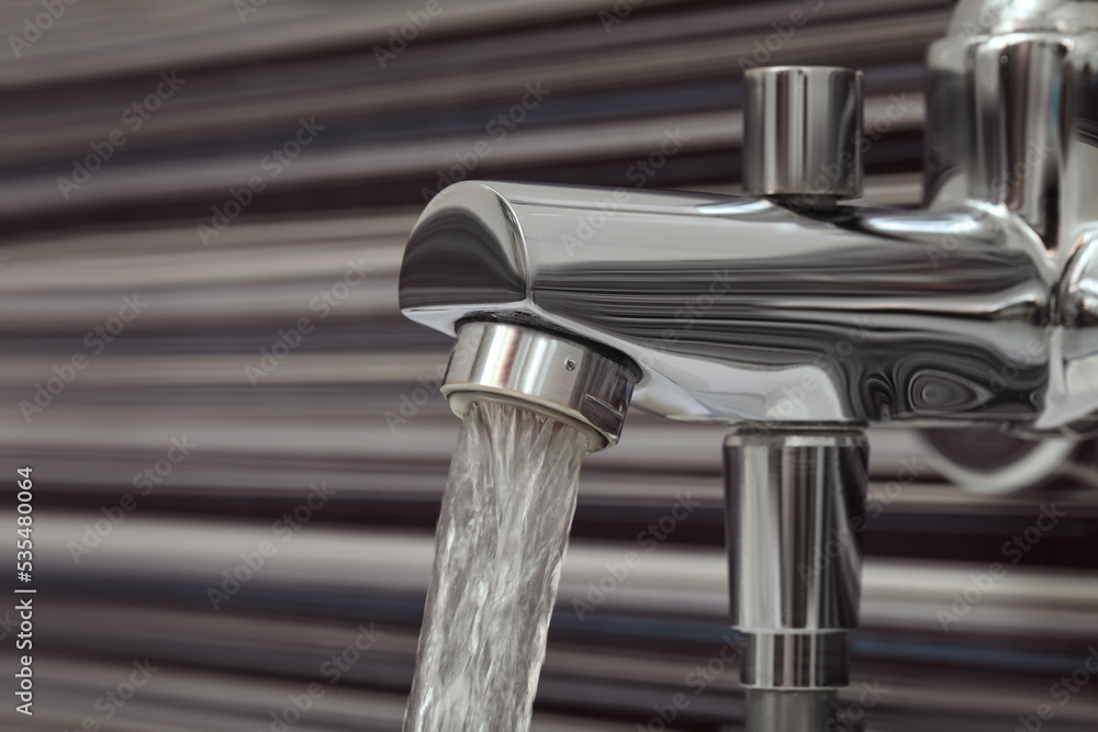 Water flowing from bath tap on blurred background, closeup Water flowing from bath tap on blurred background, closeup