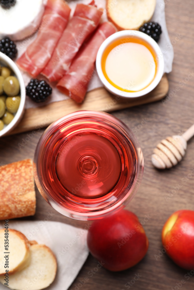 Glass of delicious rose wine and snacks on wooden table, flat lay