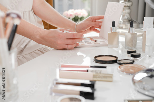 Make-up table  decorative cosmetics for professional and home makeup. Close-up view of brushes  eyeshadow palates in white sunny salon. Beauty Artists hands choosing color of base. Copy space