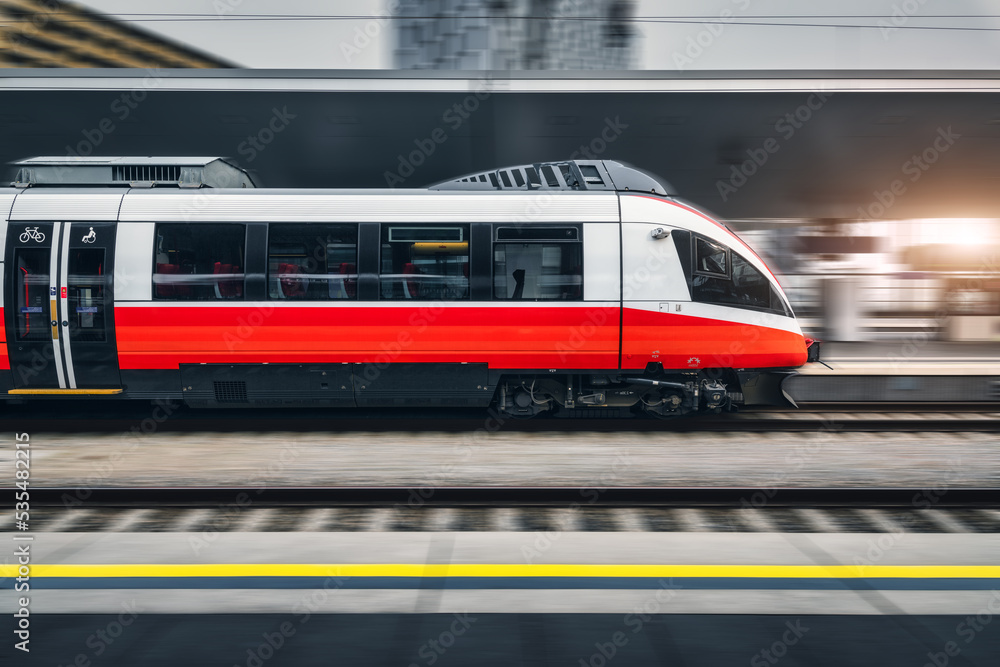 Naklejka premium High speed train in motion inside modern train station in Vienna. Fast red intercity passenger train with motion blur effect. Railway platform. Railroad in Europe. Commercial transportation. Transport
