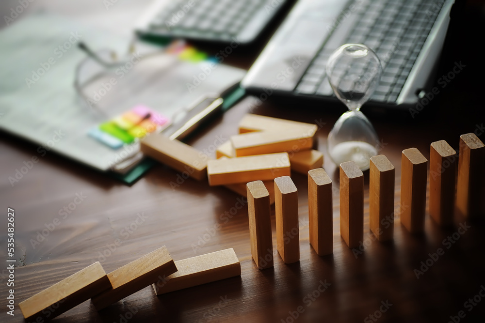 domino effect concept with wooden tiles blocked by hourglass with background domino effect concept with wooden tiles blocked by hourglass with background