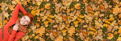 Ginger hair woman lying on autumn leaves, copy space