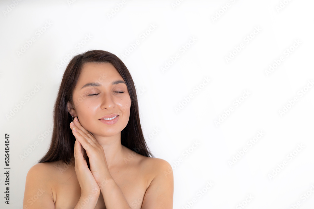 A natural portrait of a well-groomed young brunette woman with nude makeup. Gentle Beauty keeps her hands close to her face. White background place for text A natural portrait of a well-groomed young brunette woman with nude makeup. Gentle Beauty keeps her hands close to her face. White background place for text