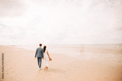 Wedding on the beach. Wedding at the North Sea on the beach. Bride and groom walk along the beach together. Image with grain in boho style