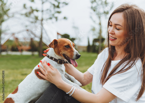 A woman in a white T-shirt and jeans hugs her Jack Russell Terrier dog in nature in the park. Loyal best friends since childhood. Lifestyle.