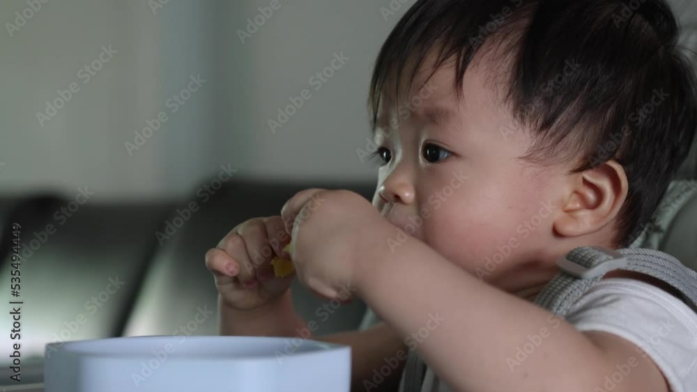 Joyful Asian Chinese baby boy holding food with dirty face during having lunch