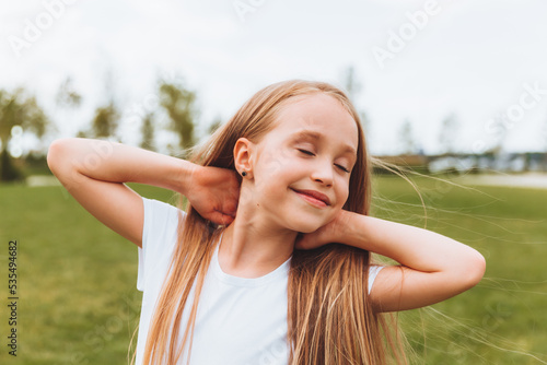 Charming happy little girl with blonde hair outdoors in the park. Portrait of a Caucasian child enjoying the sun.