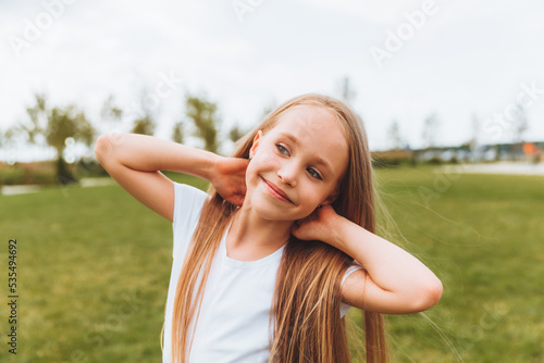 Charming happy little girl with blonde hair outdoors in the park. Portrait of a Caucasian child enjoying the sun.