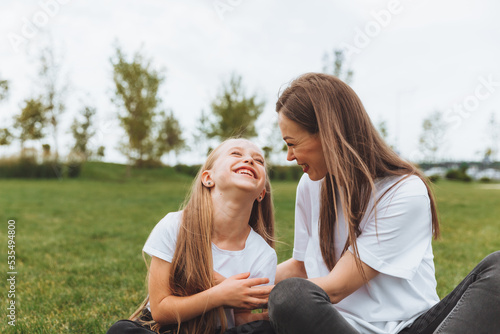 A happy mother and her daughter are sitting on the grass in the park and hugging. mother and daughter. family.joyful mom and little girl