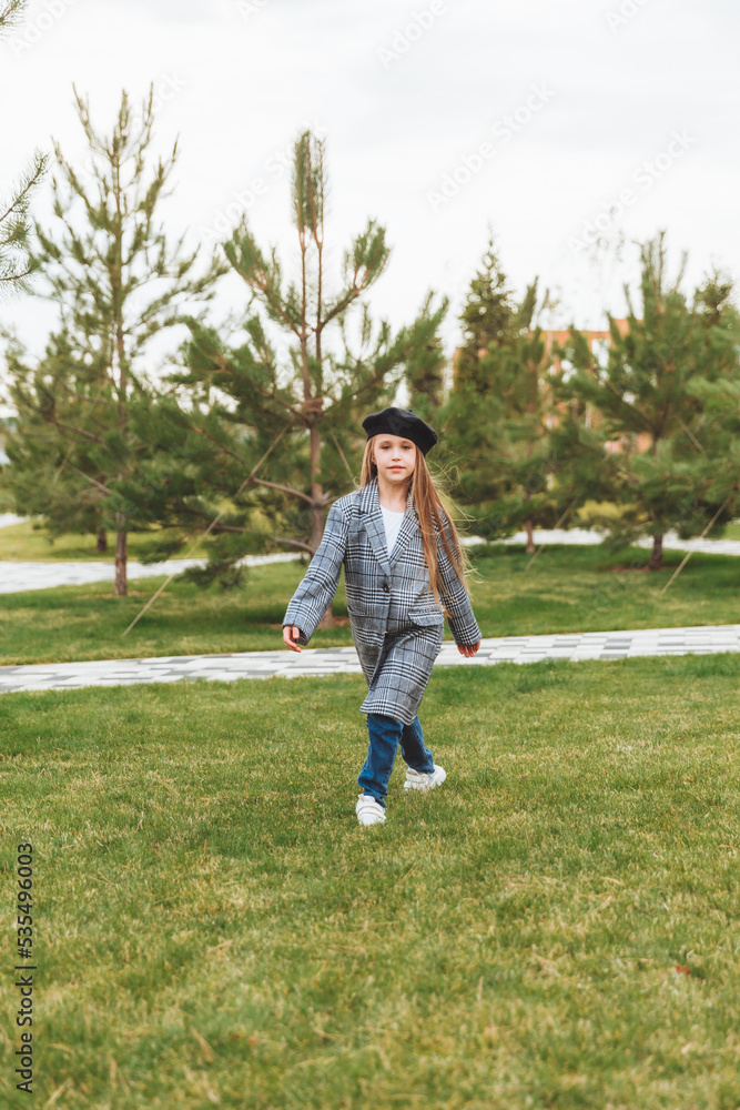 A beautiful smiling little girl with blue eyes in an autumn coat and beret poses in the park.