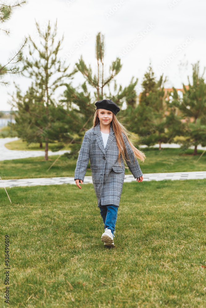A beautiful smiling little girl with blue eyes in an autumn coat and beret poses in the park.