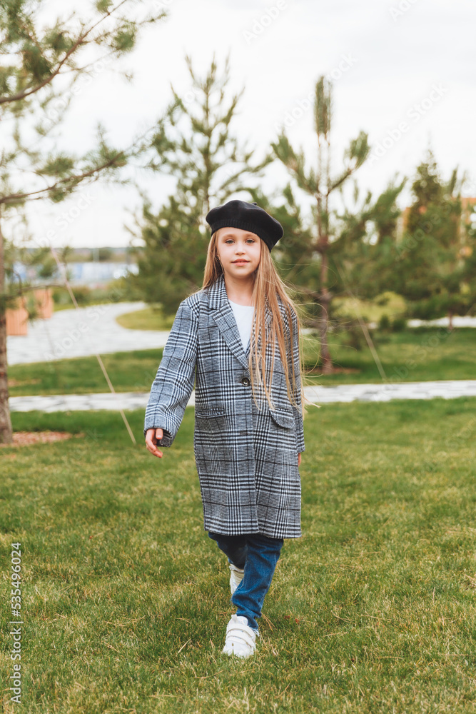 A beautiful smiling little girl with blue eyes in an autumn coat and beret poses in the park. A beautiful smiling little girl with blue eyes in an autumn coat and beret poses in the park.
