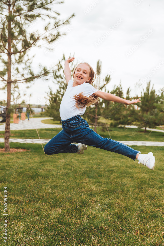 A little girl with long hair jumps having fun on the street. The concept of a happy childhood.