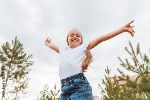 A little girl with long hair jumps having fun on the street. The concept of a happy childhood.